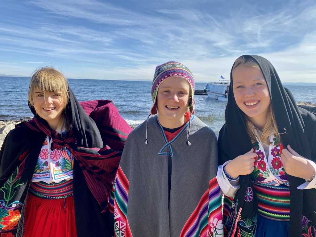 Drie jongeren in kleurrijke traditionele kleding aan het Titicacameer in Peru tijdens een familiereis.