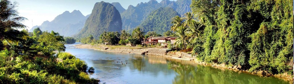 Rivierlandschap in Laos met palmbomen, dorp en karstbergen tijdens groepsrondreis Laos & Cambodja.