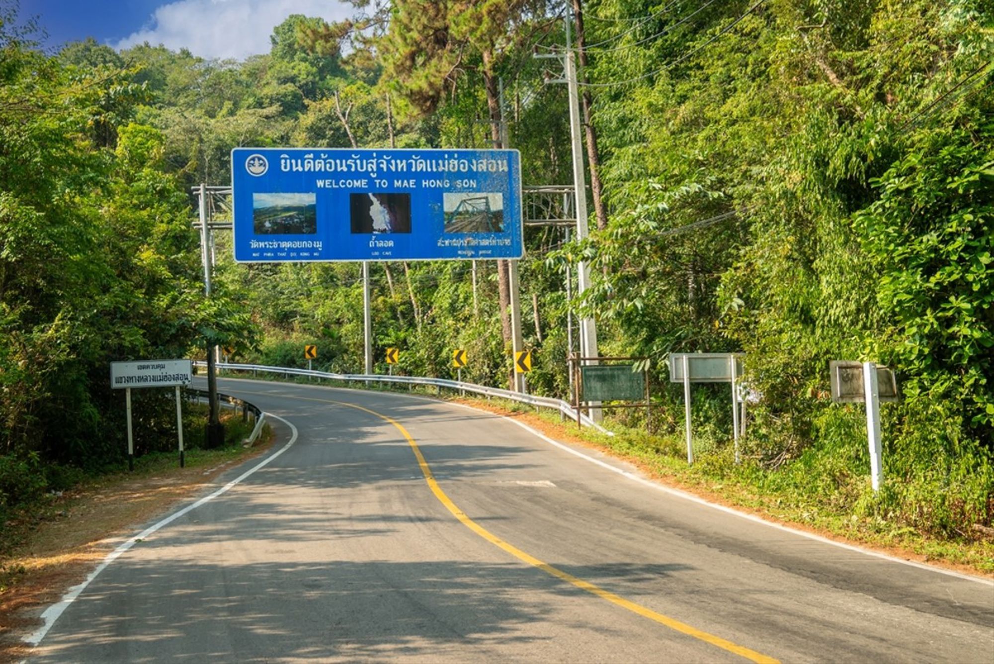 Bochtige bergweg in Thailand met verkeersbord “Welcome to Mae Hong Son” tussen dicht groen.