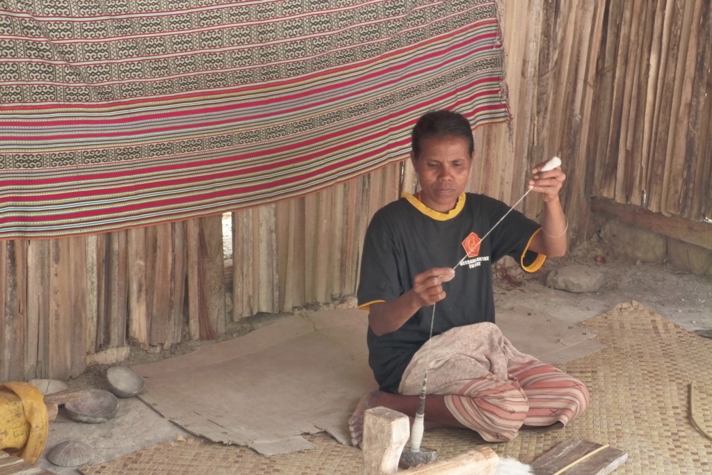 Man op Timor spint draad met een handspil in een traditionele woning tijdens rondreis Timor, Sumba & Bali.