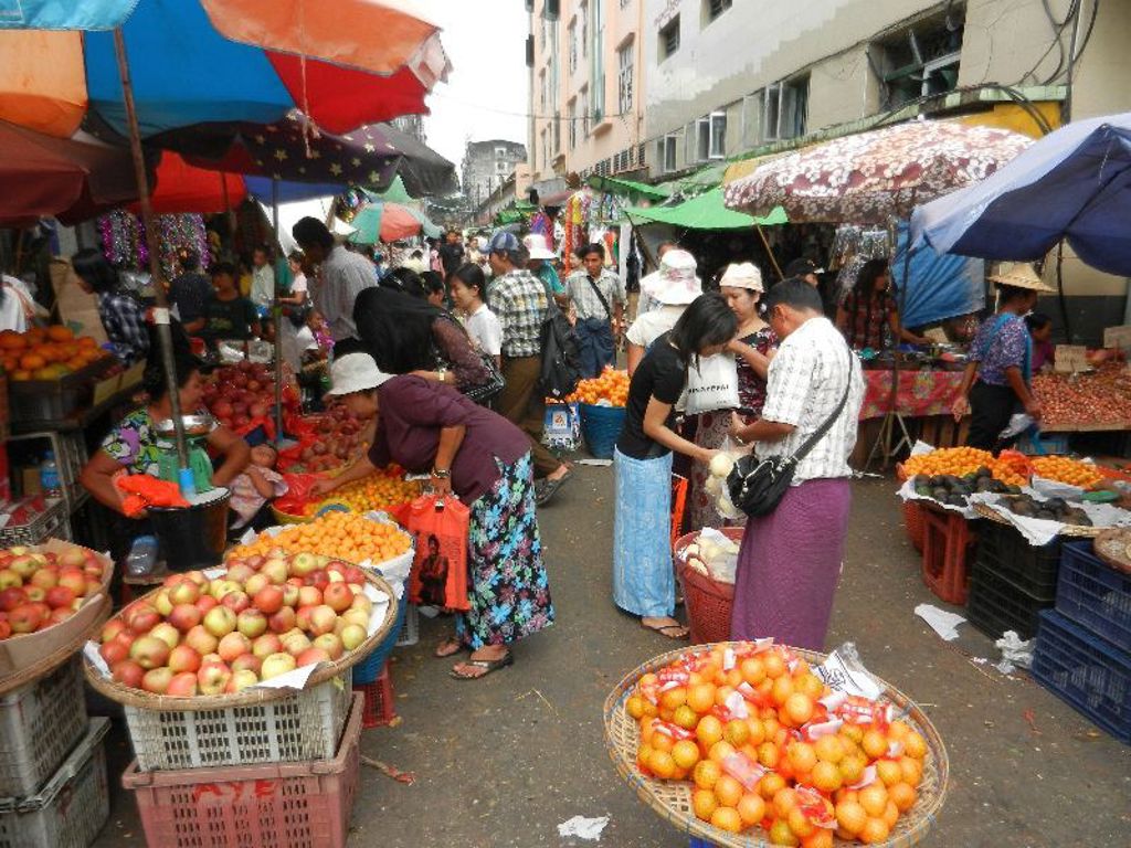 Drukke markt in Myanmar met kleurrijke parasols en kramen vol fruit.