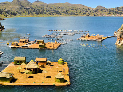 Rieteilanden van de Uros op het Titicacameer in Peru, met boten en rotsformatie in helderblauw water.