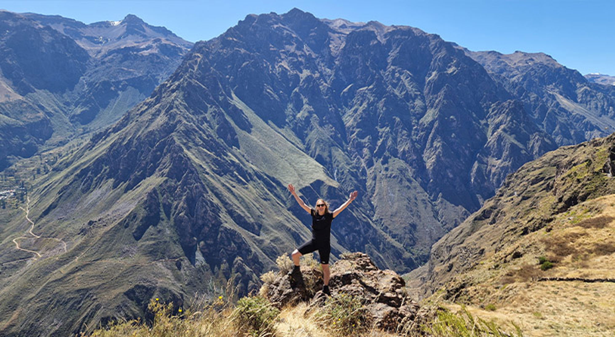 Colca Canyon Wandelaar met opgeheven armen op rots met uitzicht op ruige bergketen en diepe vallei.