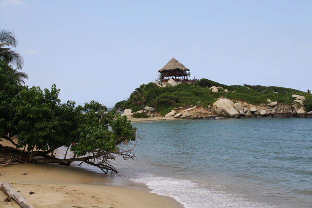 Caribisch strand in Colombia met rustig zeewater en een uitkijkpunt met rieten dak op een groen eilandje.