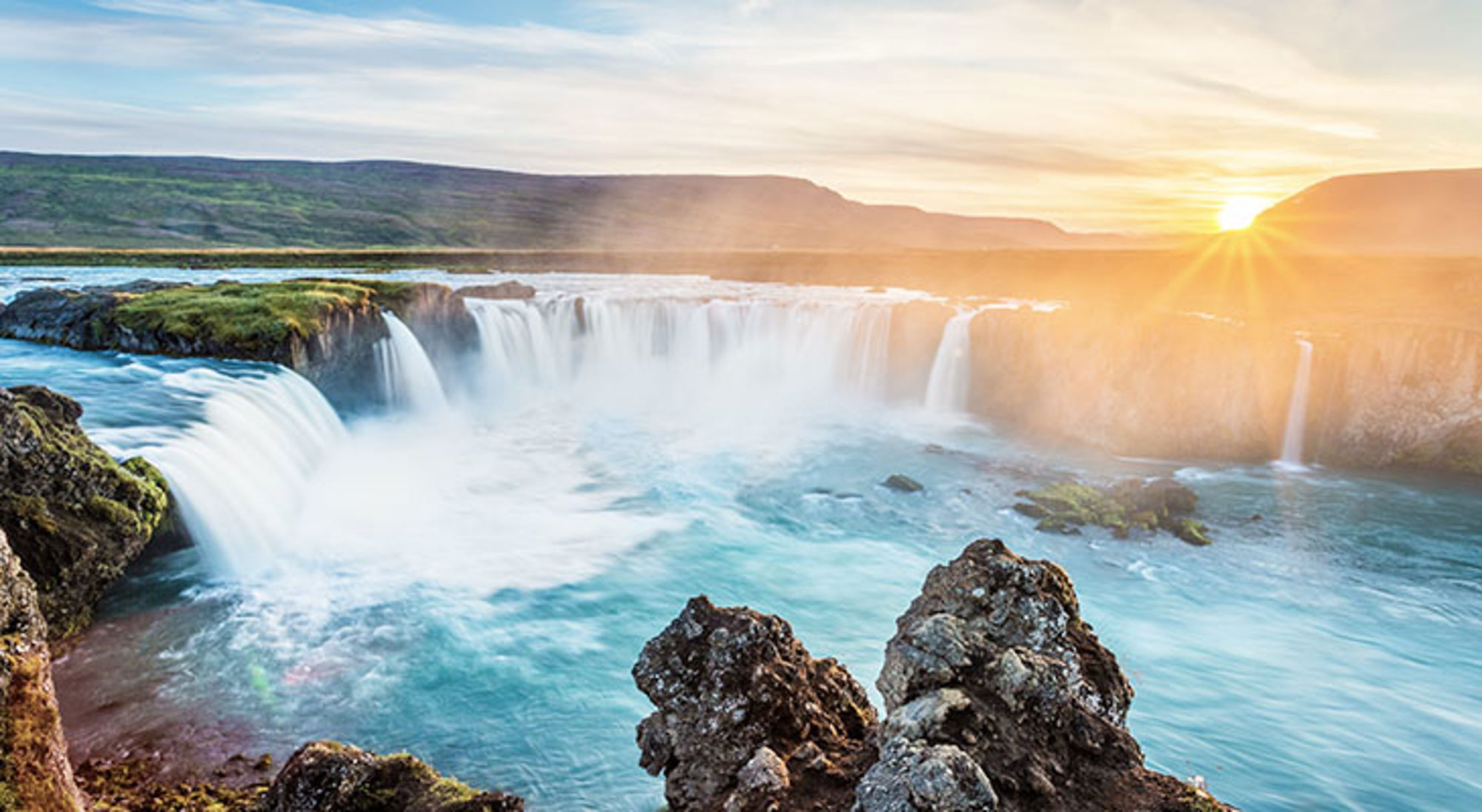Waterval in een breed rivierlandschap bij zonsondergang.