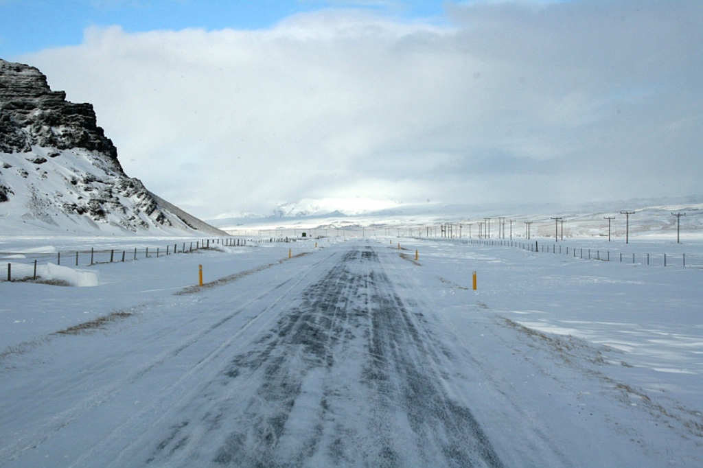Besneeuwde weg door het winterlandschap van IJsland tijdens een groepsrondreis, met bergen en eindeloze vlaktes.