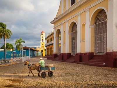 Paardenkar op kasseien langs kleurrijke gebouwen en kerk op het centrale plein van Trinidad, Cuba.