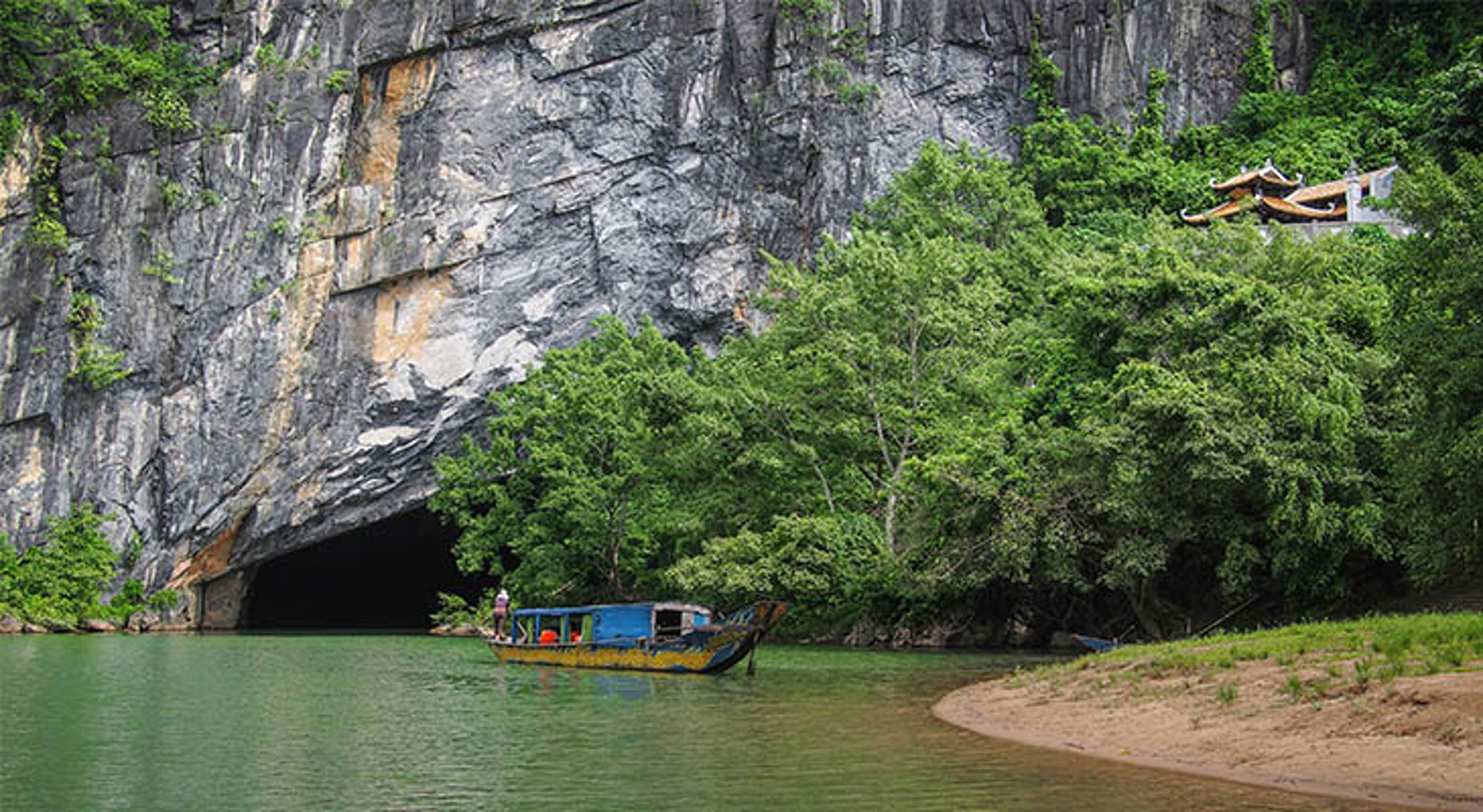 Hang son Doong Boot vaart langs een grotopening in kalkstenen rotswand met groen water en jungle, Vietnam.