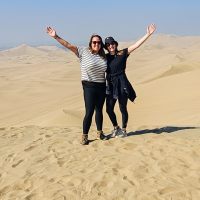 Twee reizigers op zandduinen in Peru met armen omhoog tijdens een 22-35ers groepsreis.