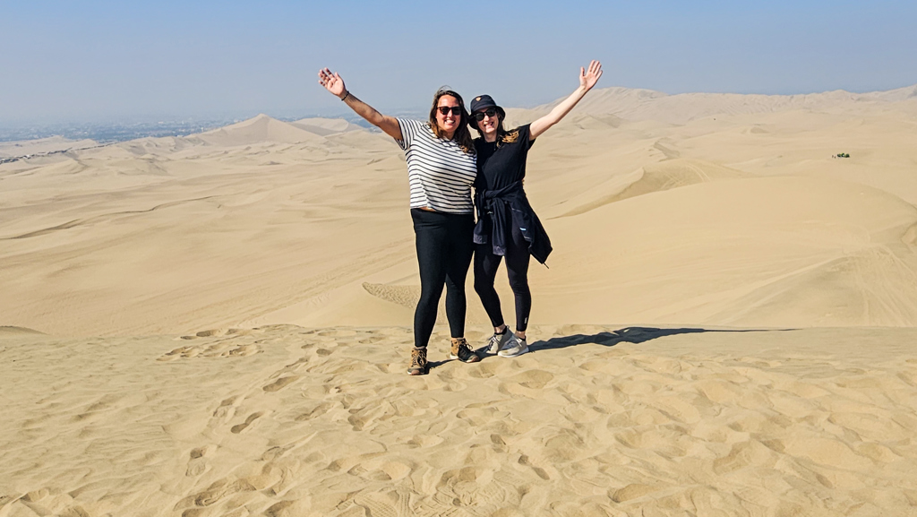 Twee reizigers op zandduinen in Peru met armen omhoog tijdens een 22-35ers groepsreis.