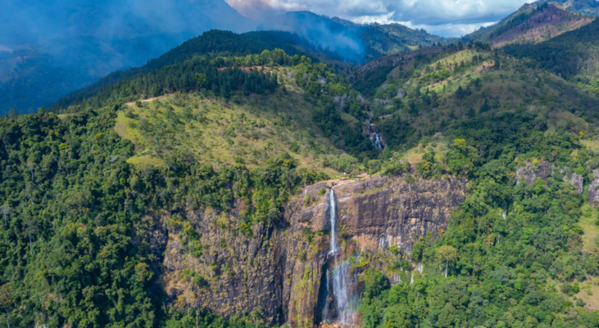 Landschap met waterval in Sri Lanka Waterval in een groene bergvallei met rotswand en wolken boven de heuvels.