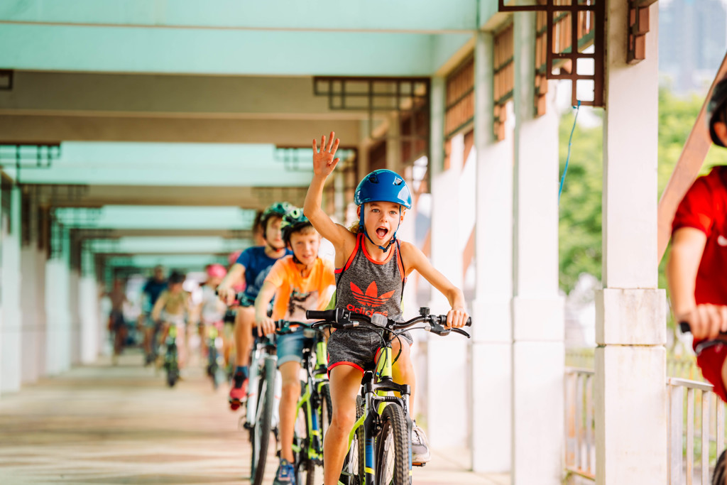 Kinderen fietsen met helm door een overdekte gang tijdens een familiereis in Thailand.