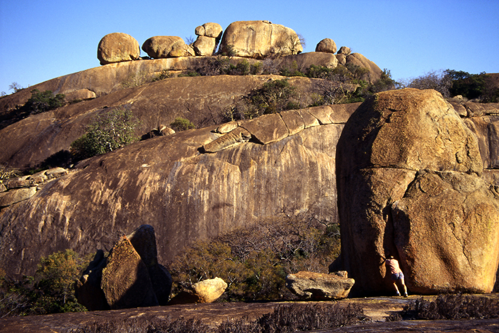 Rotsformatie met grote granieten keien in Zimbabwe, met wandelaar aan de voet van een rotswand.