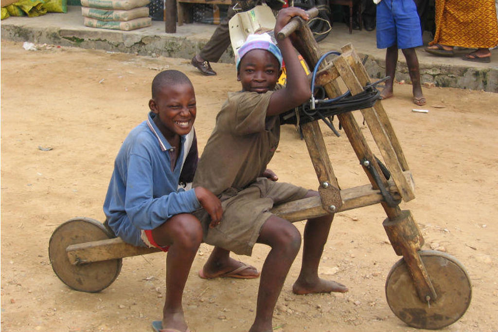 Twee kinderen spelen op een zelfgemaakte houten fiets in Uganda tijdens een groepsrondreis.