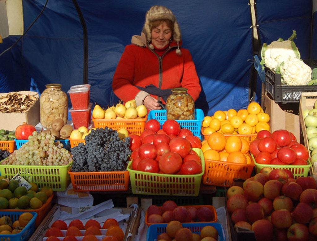 Marktkoopvrouw in Rusland achter kraam met vers fruit, groenten en ingelegde producten.