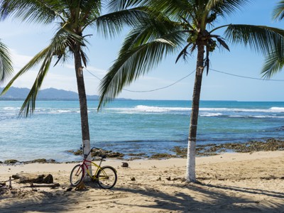 Palmbomen en fiets op het strand aan de kust van Costa Rica, met golven en bergen op de achtergrond.