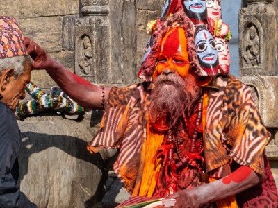Sadhu met oranje gezichtsbeschildering en kleurrijke hoofdtooi bij een tempel in Noord-India.