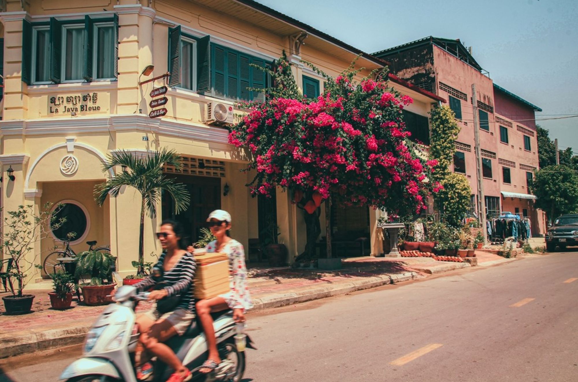 Straatbeeld in Phnom Penh met scooter, kleurrijke gevels en bloeiende bougainvillea.