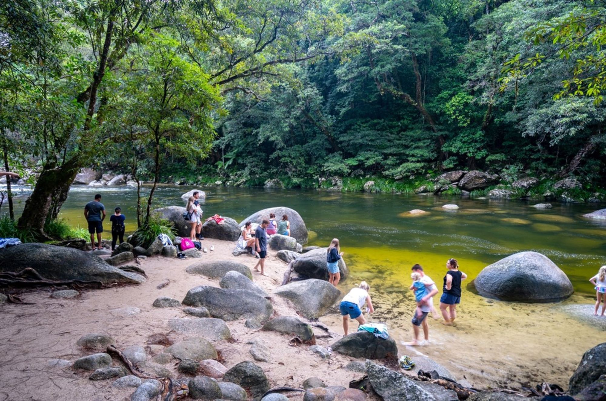 Bezoekers bij een ondiepe rivier met grote rotsblokken in het regenwoud van Australië.