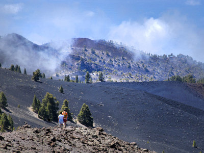 Wandelaars op een vulkanisch pad door zwarte lavavelden op Tenerife, met bergen en wolken op de achtergrond.