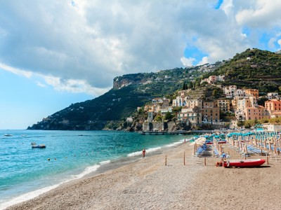 Strand met ligbedden en kleurrijke huizen tegen de heuvels aan de Amalfikust, Italië.