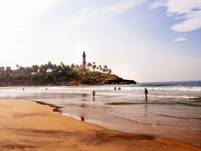 Strand bij Kovalam met vuurtoren, palmbomen en mensen in de branding, Zuid-India.