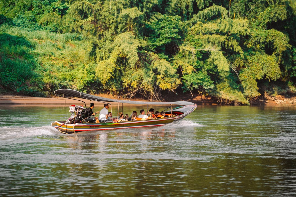 Longtailboot met reizigers op een rivier in Thailand, langs groene jungle tijdens een familiereis.