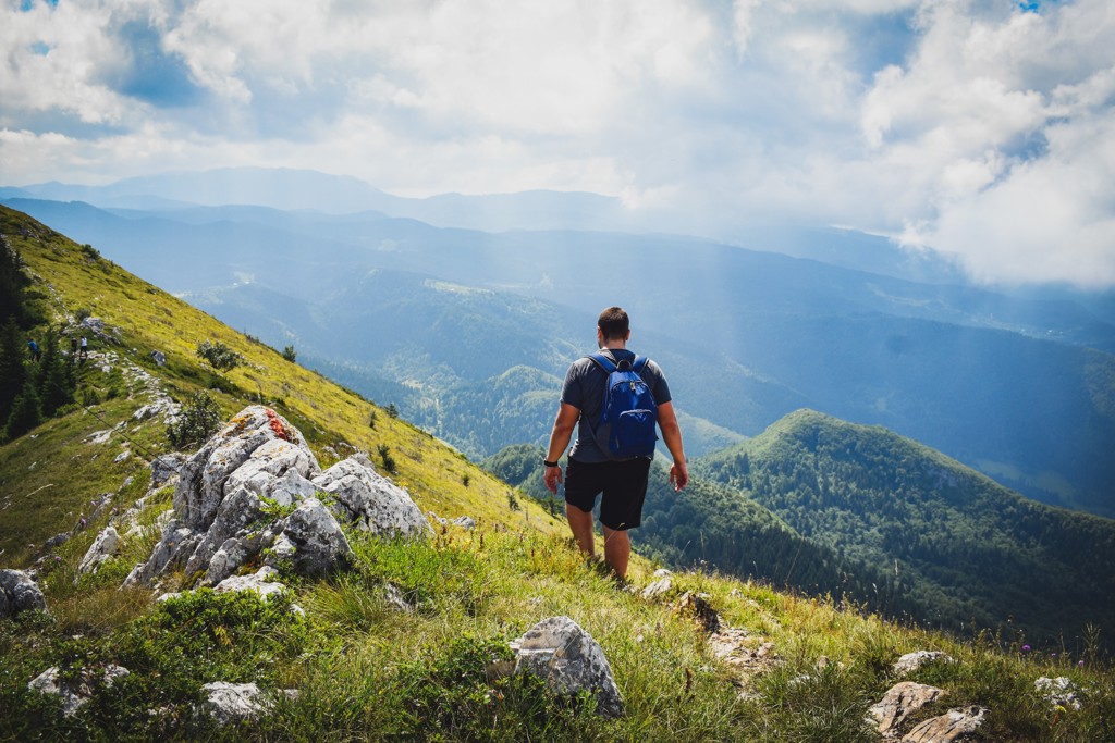 Wandelaar met rugzak op bergpad met uitzicht over groene valleien in Bosnië en Herzegovina.