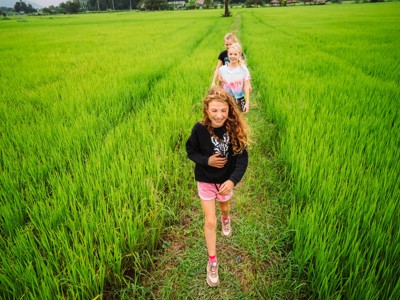 Kinderen wandelen door groene rijstvelden tijdens de Route Thailand Noord en Zuid.