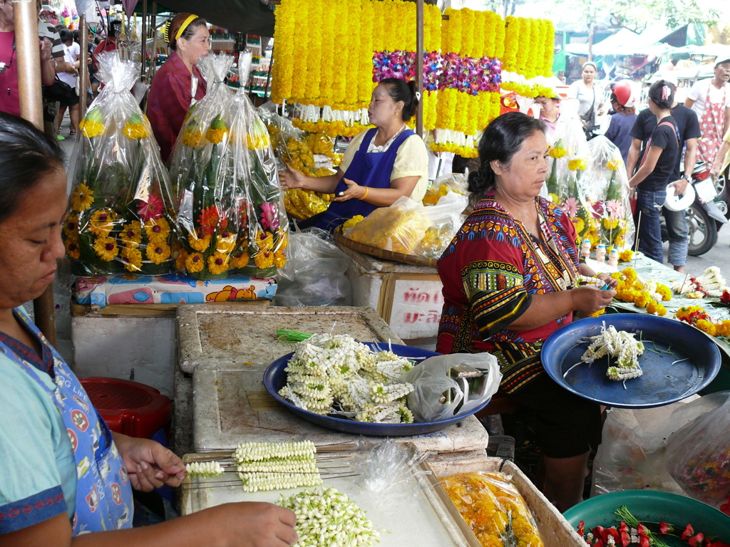 Bloemenmarkt in Thailand met verkopers die jasmijn- en goudsbloemenslingers maken en verkopen.