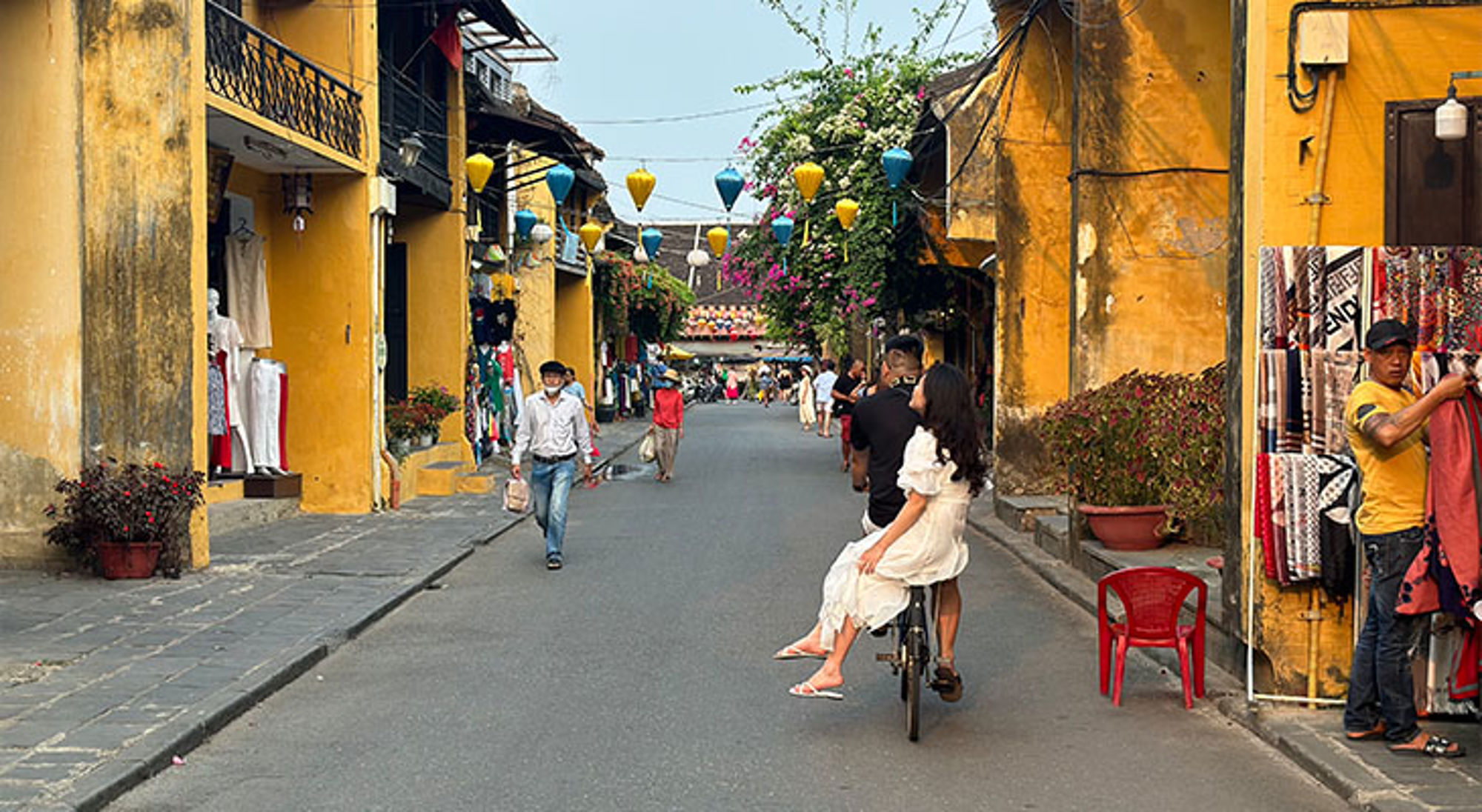 Hoi An Vietnam Straat in Hoi An met gele gevels, kleurrijke lampionnen en fietsers tussen winkels en marktkramen.