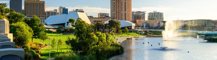 Skyline van Adelaide met de River Torrens, groene parken en een fontein bij zonlicht.