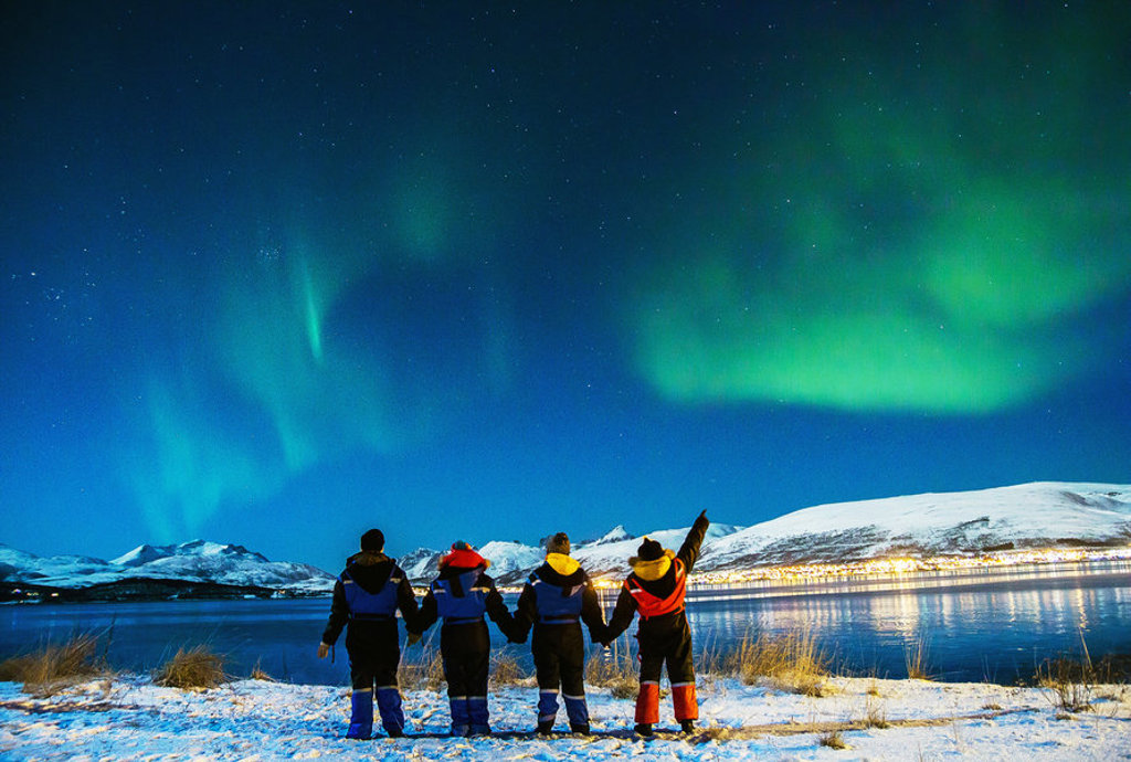 Noorderlicht boven Noord-IJsland, met reizigers aan de kust bij besneeuwde bergen.