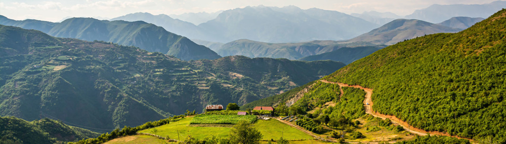 Berglandschap in Albanië met groene heuvels, slingerende weg en uitzicht op de bergen.