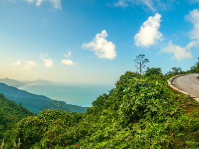 Kustweg langs groene heuvels met uitzicht op zee tijdens de Route Indochina-reis.