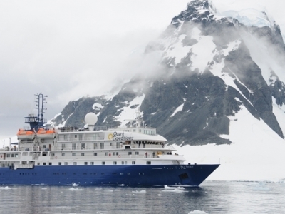 Expeditiecruiseschip bij besneeuwde bergkust in Antarctica tijdens Route Crossing the Circle.