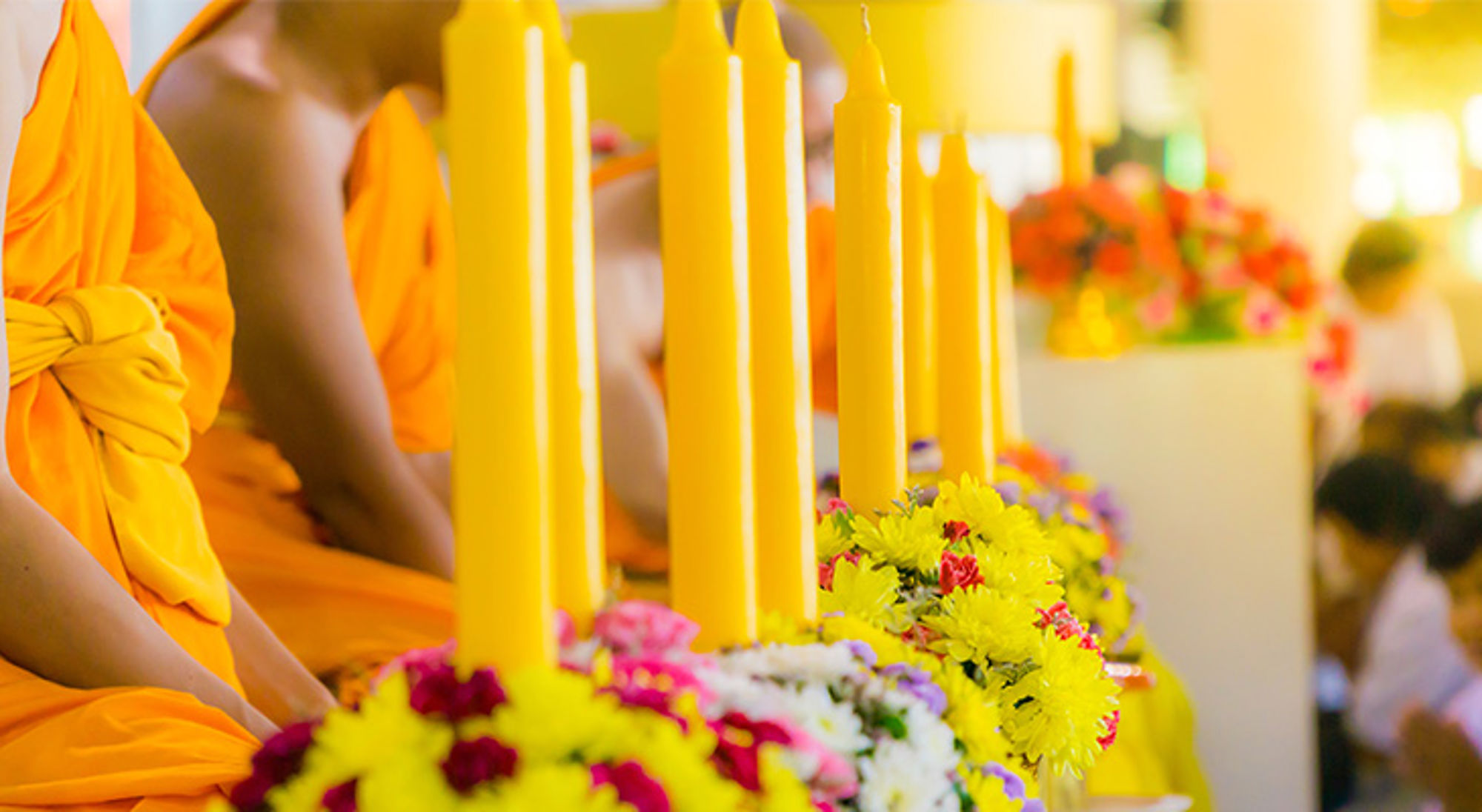 Asanha Bucha Dag en boeddhistische vastendag Boeddhistische monniken in oranje gewaden naast gele kaarsen en kleurrijke bloemen tijdens een ceremonie.