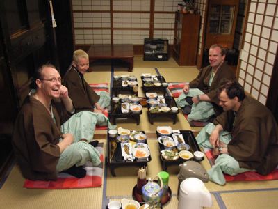 Reizigers in yukata eten een traditioneel Japans diner aan lage tafels in een tatami-kamer.