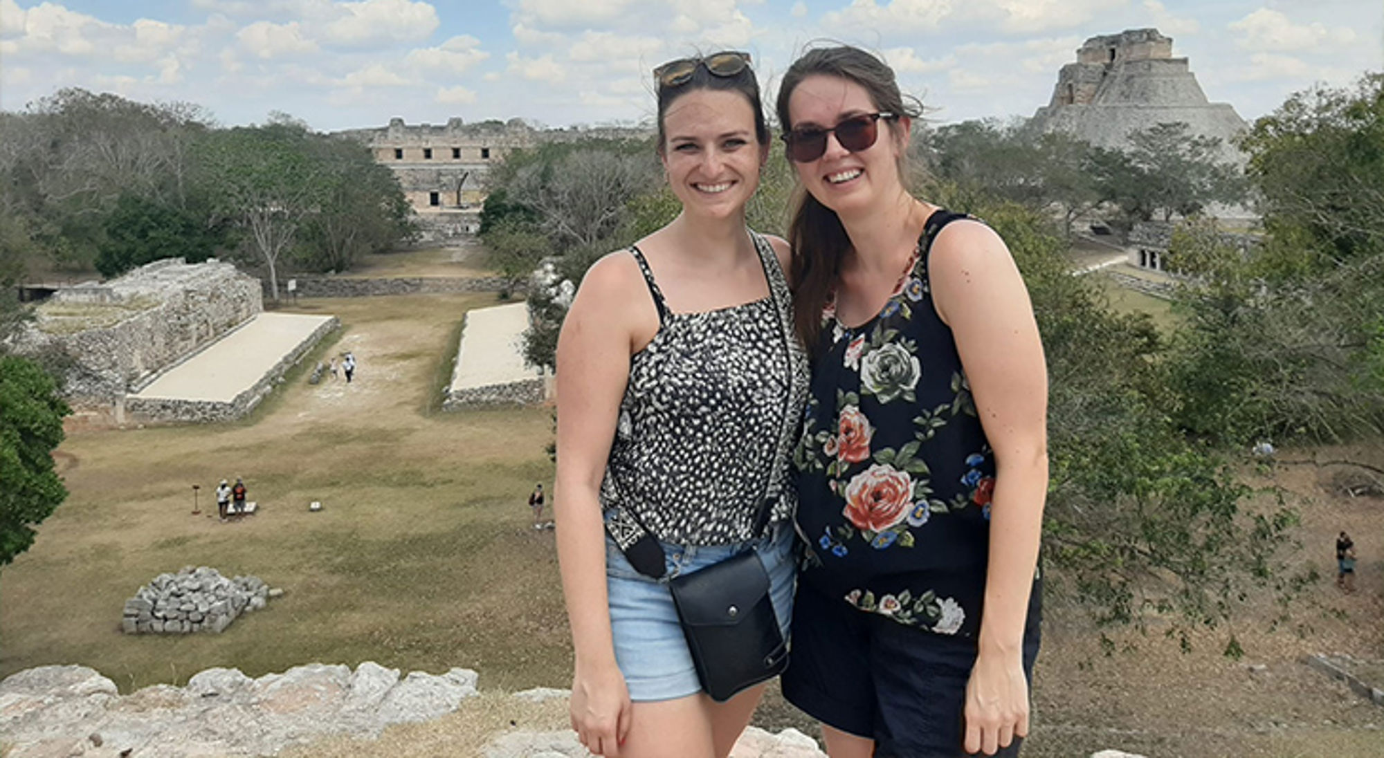 Fleur en Elin in Mexico Twee reizigers poseren bij de Mayaruïnes van Uxmal in Mexico, met piramides op de achtergrond.