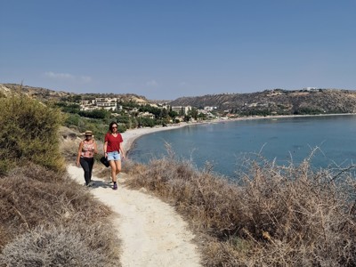 Wandelaars op kustpad langs de baai tijdens Route Cyprus, met strand en heuvels op de achtergrond.
