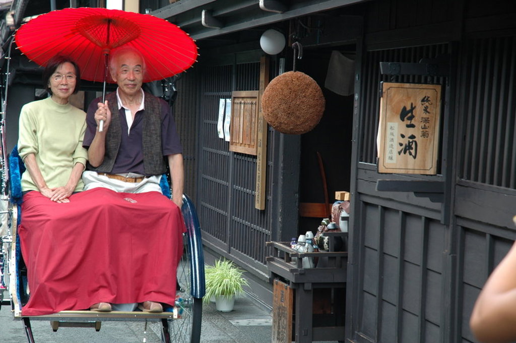 Stel in een riksja onder rode paraplu in een traditionele straat in Japan tijdens groepsrondreis Japan Hoogtepunten.