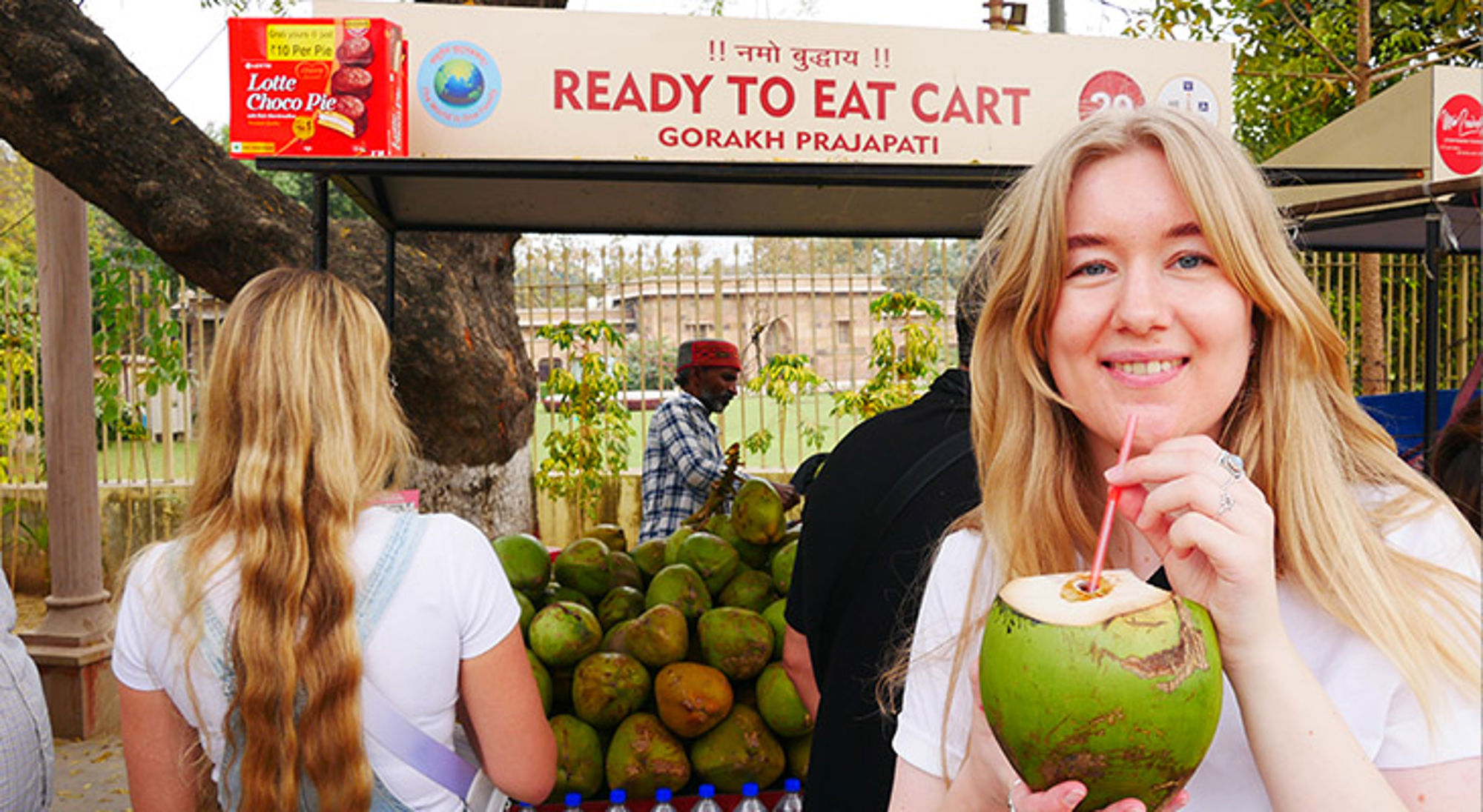 Vrouw drinkt kokoswater bij een streetfoodkraam met verse kokosnoten.