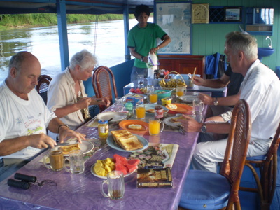 Ontbijt aan boord van een rivierboot tijdens de route Kalimantan, met fruit, toast en sap op tafel.