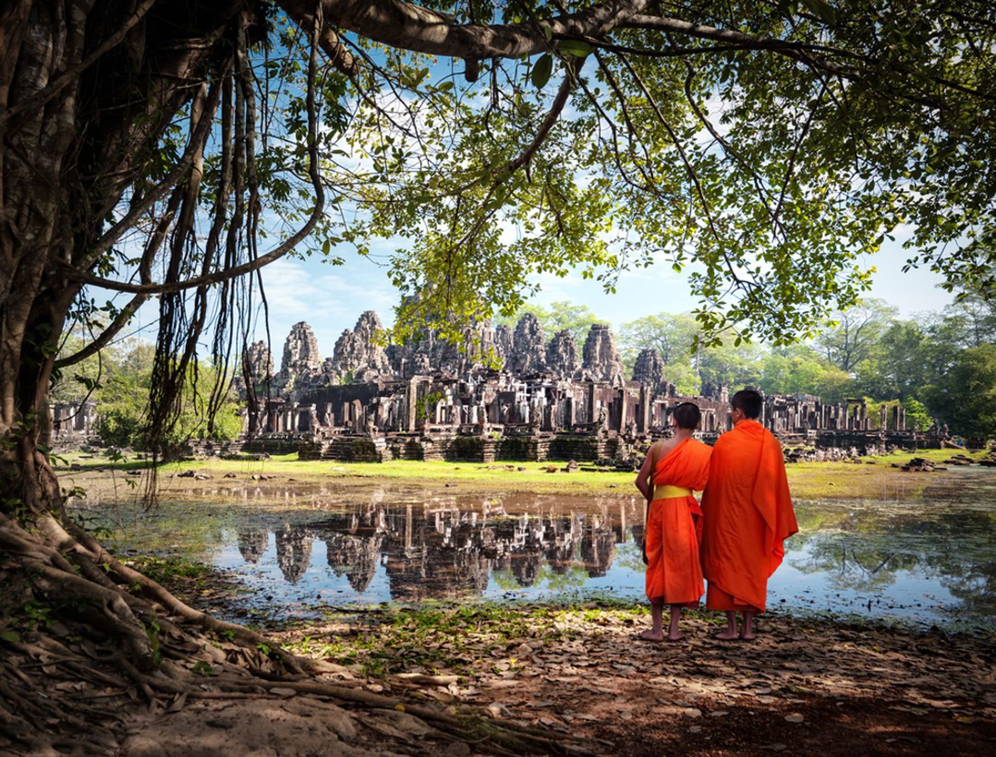Twee boeddhistische monniken kijken uit over Angkor Thom bij Angkor Wat, met spiegeling in het water, Cambodja.