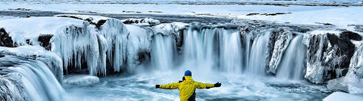 Reiziger in gele jas bij bevroren waterval in IJsland.