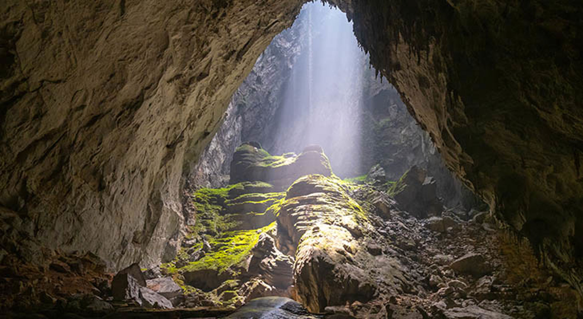 Hang son Doong Zonlicht dat door een grotopening valt op rotsen en mos in een grot in Vietnam.
