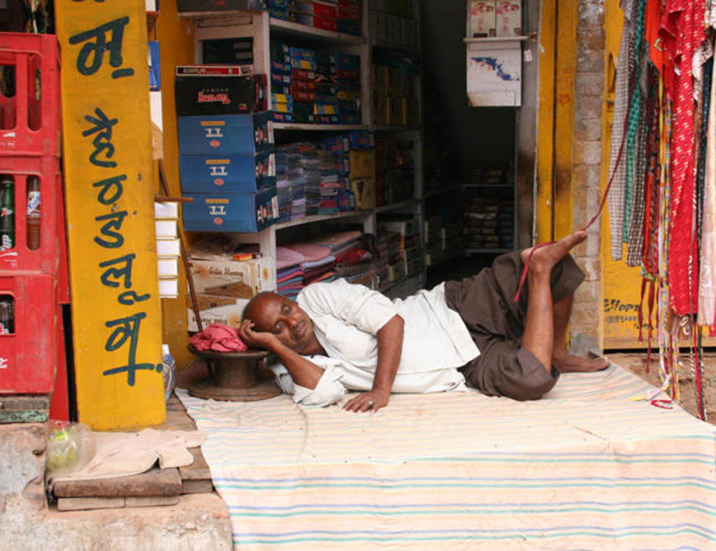 Man rust uit op een mat voor een winkel in Zuid-India, tijdens een groepsrondreis langs hoogtepunten.