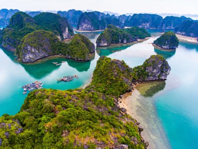 Karstrotsen en groene eilandjes in Halong Bay, Vietnam, met turquoise water en drijvende vissersdorpjes.