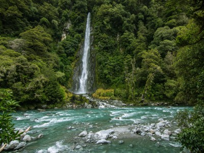 Hoge waterval in dicht regenwoud aan een turquoise rivier op Nieuw-Zeeland.
