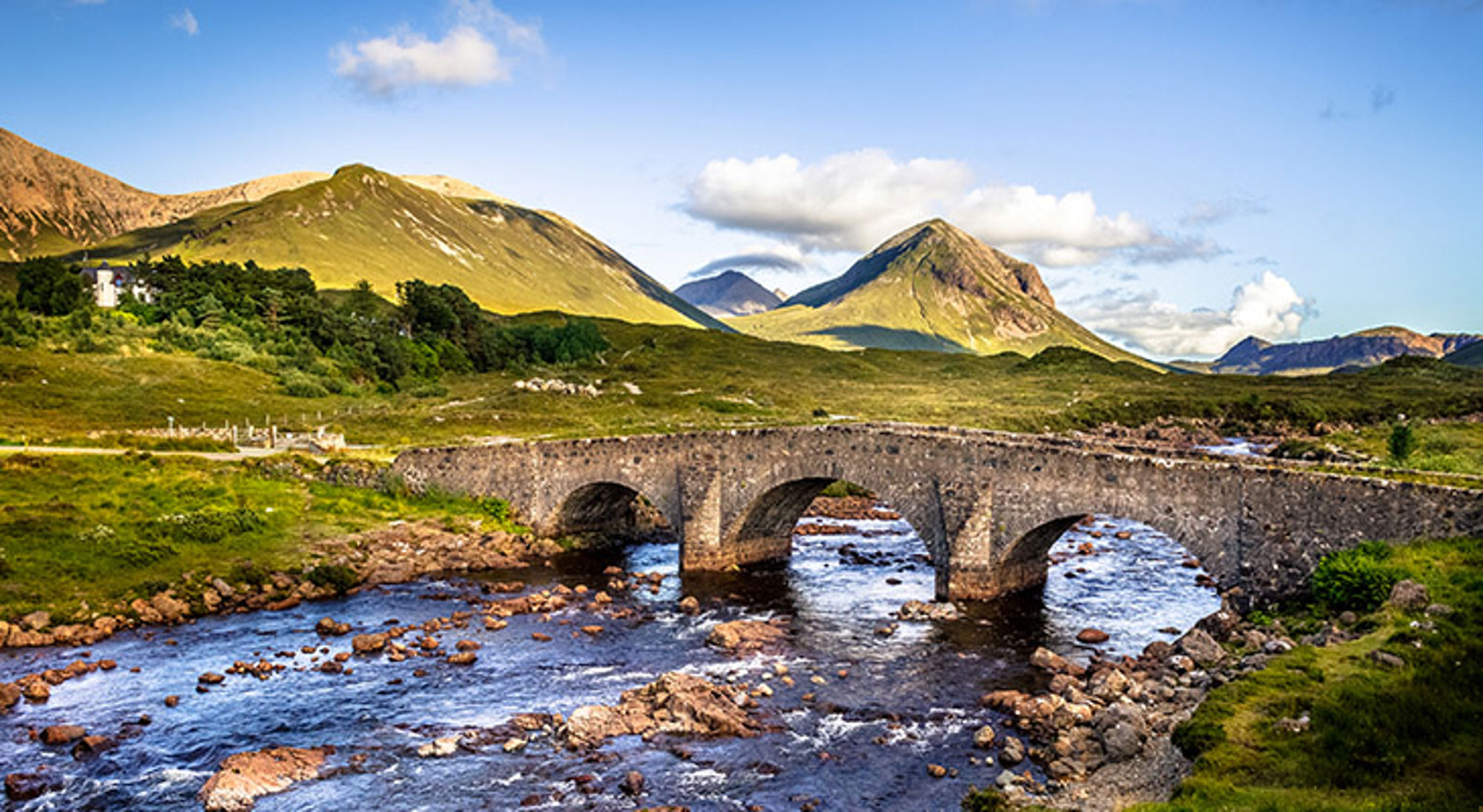 schotland-isle-of-skye Stenen boogbrug over een rivier met bergen op de achtergrond in Schotland.